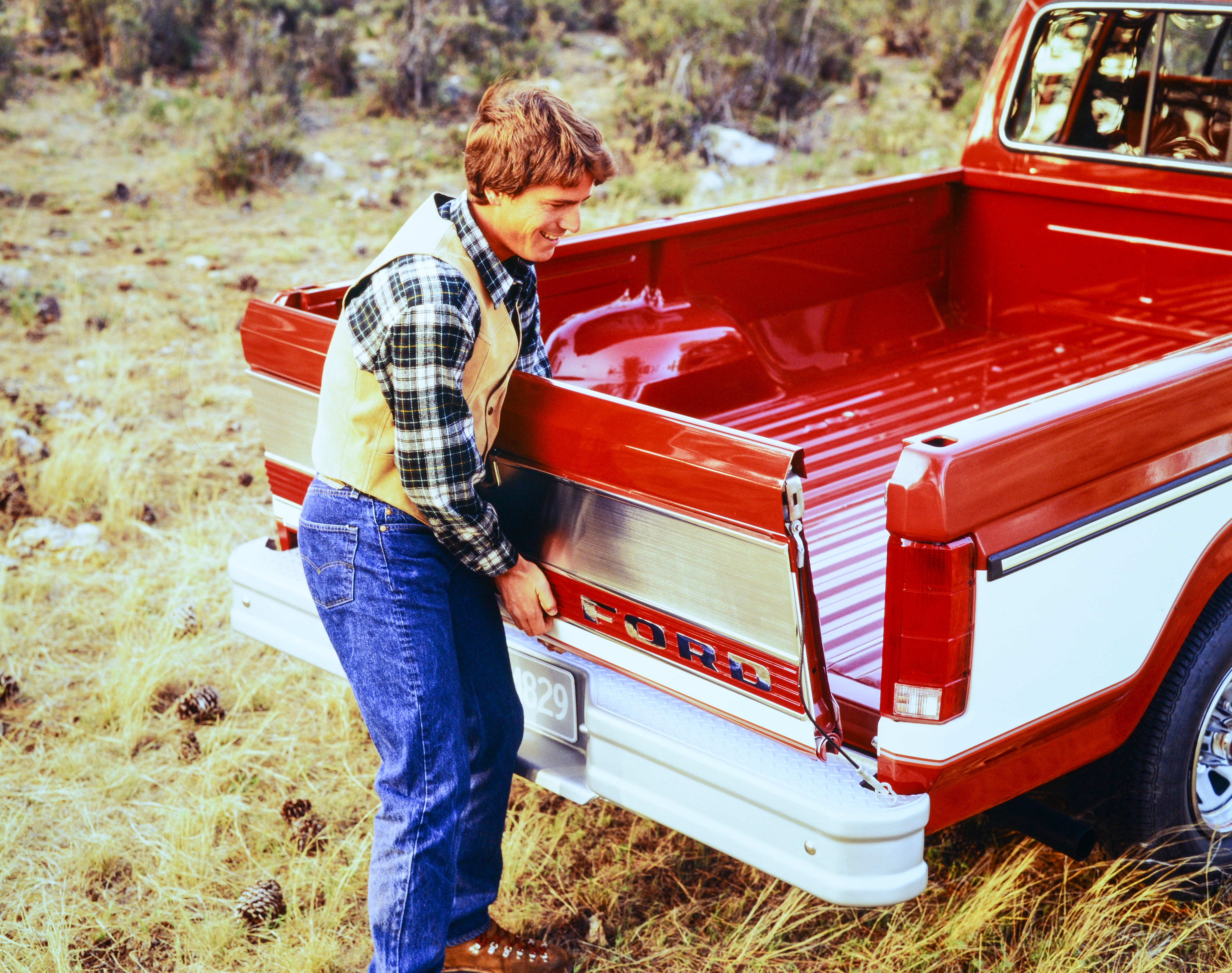 A man opens the tailgate of a red 1985 F-150